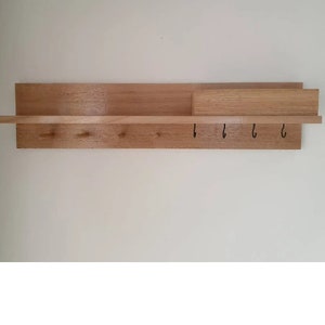 May include: A wooden wall-mounted shelf with a natural finish. It features a long shelf, a smaller shelf section, and a row of hooks. The shelf is designed for storage and organization, perfect for entryways or hallways.