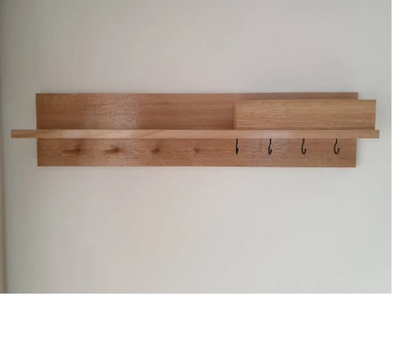 May include: A wooden wall-mounted shelf with a natural finish. It features a long shelf, a smaller shelf section, and a row of hooks. The shelf is designed for storage and organization, perfect for entryways or hallways.