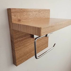 K&ouml;nnte beinhalten: Ein Holzregal mit einem verchromten Toilettenpapierhalter. Das Regal ist aus hellbraunem Holz mit nat&uuml;rlicher Maserung.