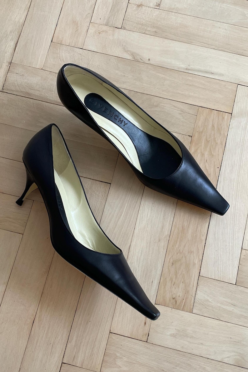 K&ouml;nnte beinhalten: Ein Paar schwarze, spitze Pumps aus Leder mit einem Stiletto-Absatz. Die Schuhe haben ein schlichtes Design und sind aus hochwertigem Leder gefertigt. Der Markenname "Givenchy" ist auf der Innensohle eines Schuhs sichtbar.