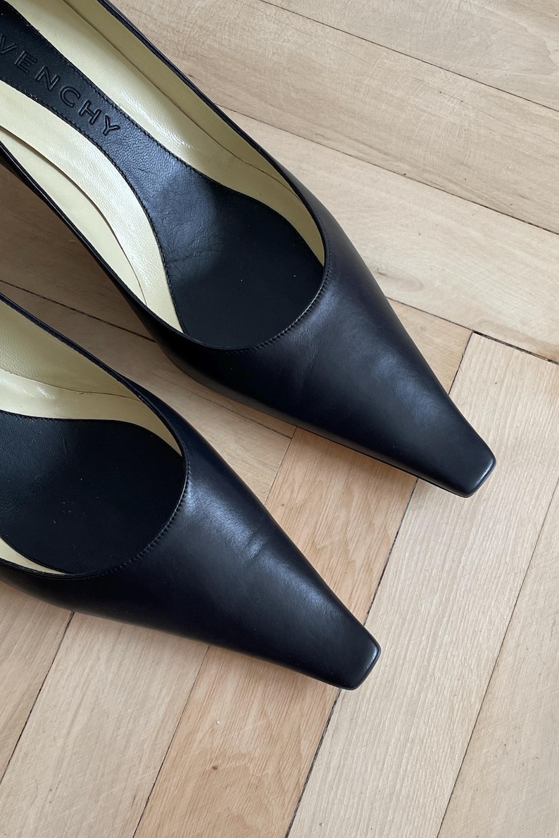 K&ouml;nnte beinhalten: Ein Paar schwarze, spitze Pumps aus Leder mit niedrigem Absatz. Die Schuhe haben ein schlichtes Design und sind aus hochwertigem Leder gefertigt. Der Markenname "Givenchy" ist auf der Innensohle eines Schuhs sichtbar.