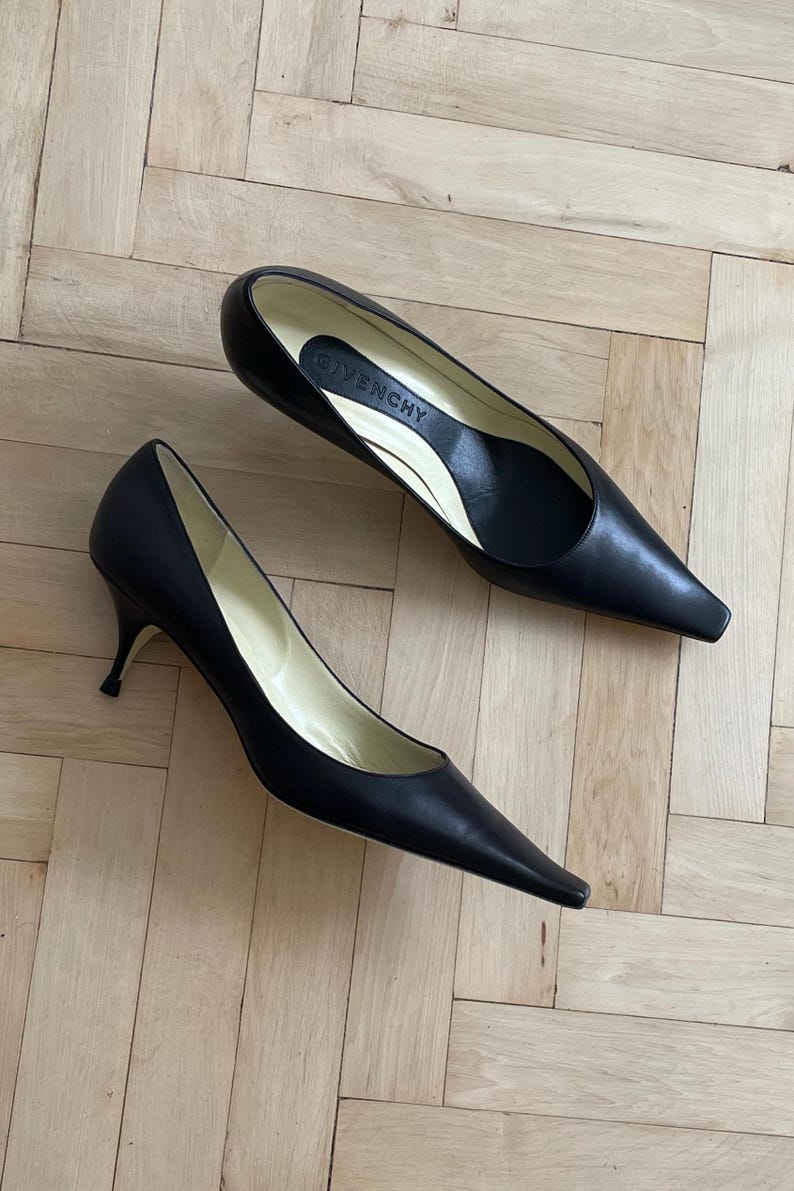 K&ouml;nnte beinhalten: Ein Paar schwarze, spitze Pumps aus Leder mit einem Stiletto-Absatz. Die Schuhe haben ein schlichtes Design und sind aus hochwertigem Leder gefertigt. Der Markenname "Givenchy" ist auf der Innensohle eines Schuhs sichtbar.
