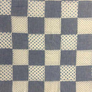 May include: A quilt featuring a checkerboard pattern of alternating squares. One set of squares is solid denim blue, while the other set is white with a repeating pattern of small, dark blue polka dots arranged in a grid across the fabric surface.