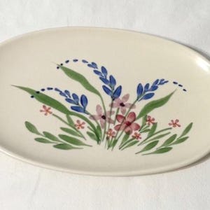 May include: Oval ceramic serving platter with a hand-painted floral design. The flowers are in shades of blue, pink, and red, with green leaves. The platter has a cream-colored background.