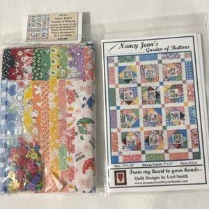 May include: A quilting kit titled Nancy Jean's Garden of Buttons containing assorted colorful patterned fabric strips, a small bag of multicolored buttons, and a printed instruction booklet with a quilt illustration and the text Nancy Jean's Garden of Buttons.
