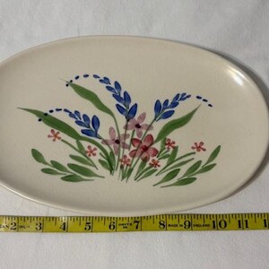 May include: Oval ceramic serving platter with a hand-painted floral design. The flowers are in shades of blue, pink, and red, with green leaves. The platter is approximately 13 inches long.
