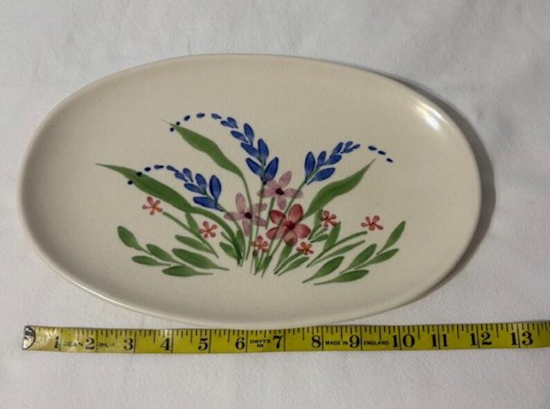 May include: Oval ceramic serving platter with a hand-painted floral design. The flowers are in shades of blue, pink, and red, with green leaves. The platter is approximately 13 inches long.
