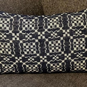 May include: A rectangular throw pillow featuring a repeating geometric pattern in dark navy blue and off-white. The woven textile design consists of interconnected squares and cross-like shapes, creating a structured, symmetrical grid across the surface.