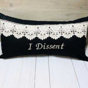 May include: Black pillow with white lace trim and the text "I Dissent" embroidered in white.
