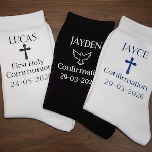 May include: Three pairs of socks, two white and one black, with religious text and dates. The white socks have a cross and the words "LUCAS First Holy Communion 24-05-2020" and "JAYCE Confirmation 29-03-2026". The black sock has a dove and "JAYDEN Confirmation 29-03-2020".