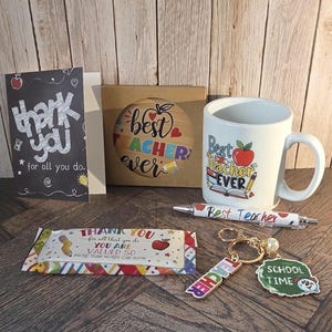 May include: A teacher appreciation gift set including a white ceramic mug with Best Teacher Ever text, a greeting card with thank you for all you do text, a boxed coaster, a Best Teacher pen, a candy bar wrapper, and a keychain with Teacher and School Time tags.