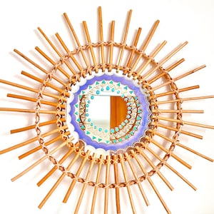 Peut inclure: Un miroir décoratif rond avec un design en forme de soleil. Le cadre est fait de bâtons de bambou de couleur naturelle rayonnant vers l'extérieur. Le miroir central a un motif peint avec des accents turquoise et or, entouré d'une bordure lavande.