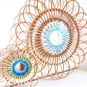Peut inclure: Deux miroirs décoratifs en rotin. Le plus grand miroir a un design circulaire avec un cadre tissé et un centre coloré de style mosaïque. Le plus petit miroir a un design similaire avec un centre bleu et vert. Les deux miroirs sont sur une surface blanche.