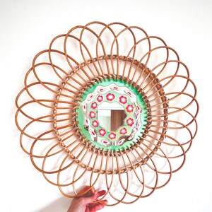 Peut inclure: Miroir rond décoratif avec un cadre en rotin tressé. Le centre du miroir présente un fond vert clair avec un motif floral rouge et blanc. Le cadre a un design en forme de fleur, d'environ 50 cm de diamètre.