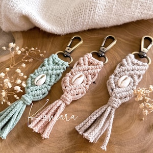 Könnte beinhalten: Drei Makramee-Schlüsselanhänger mit einem Muschel-Anhänger. Die Schlüsselanhänger sind in Grün, Rosa und Beige mit einem Quasten am unteren Ende.