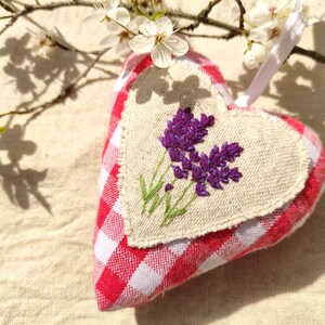 Può includere: Un cuscino a forma di cuore a quadri rossi e bianchi con un pannello di lino con fiori di lavanda ricamati.