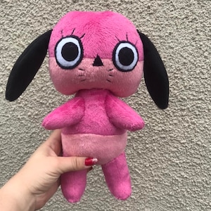 May include: Pink plush toy dog with large black eyes and black ears. The toy is standing on its own two feet.