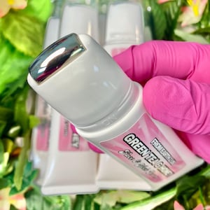 May include: White tubes of Green Tea & Honey face cream with a silver rollerball applicator. The tubes have pink labels with black text. The background includes green foliage and pink flowers.