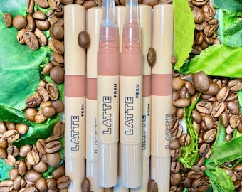 May include: A collection of six lip gloss tubes with the word "LATTE" printed on them. The tubes are beige with a pink base and are surrounded by coffee beans and green leaves. The lip gloss applicators are clear.