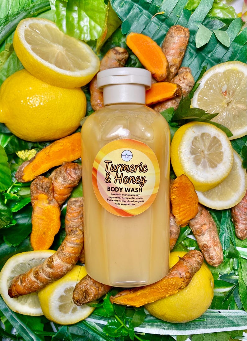 May include: A clear plastic bottle of Turmeric & Honey Body Wash. The bottle is surrounded by lemons and turmeric root.