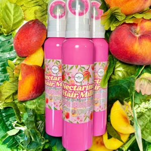 May include: Three bright pink cylindrical bottles of Nectarine Hair Milk leave-in conditioner. Each bottle features a clear pump dispenser, a white label with pink text, and a botanical illustration of nectarines and green leaves.