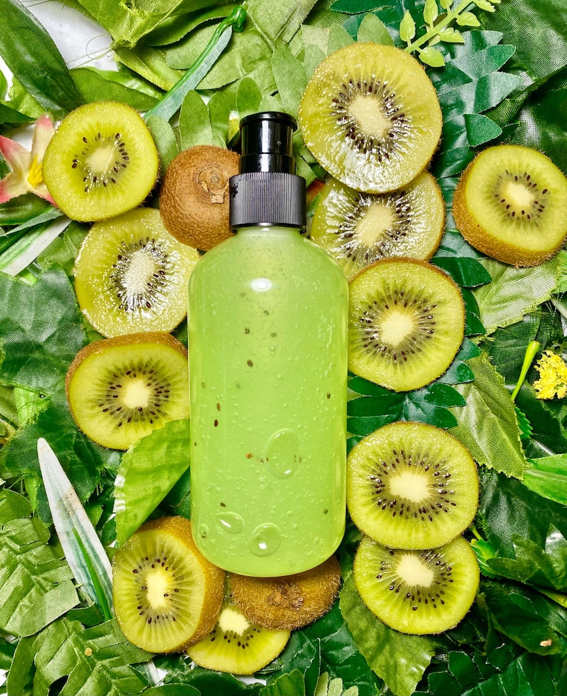 May include: A clear green bottle with a black pump top, surrounded by kiwi fruit slices on a bed of green leaves.