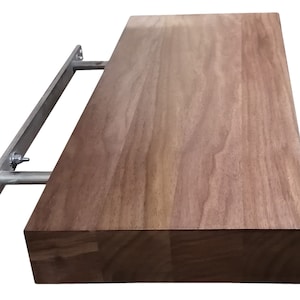Puede incluir: Una estantería de madera con un soporte metálico. La estantería es de madera oscura y tiene un acabado natural. El soporte es de metal plateado y está fijado a la pared.