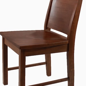 Peut inclure: Chaise en bois de couleur marron foncé. Elle possède une assise rectangulaire, quatre pieds et un dossier. Le dossier est légèrement incurvé et relié à l'assise par des supports verticaux. La chaise est en bois massif.