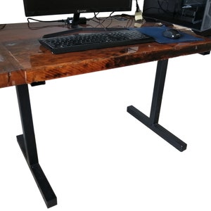 May include: A wooden desk with a dark brown epoxy resin finish. The desk has black metal legs with a T-shaped base. A computer monitor, keyboard, and mouse are on the desk.