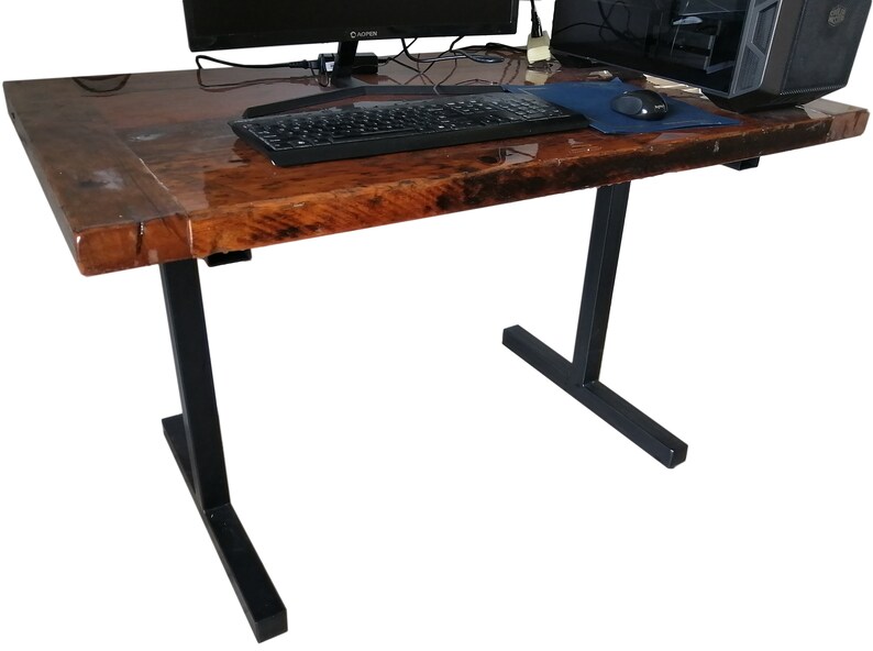 May include: A wooden desk with a dark brown epoxy resin finish. The desk has black metal legs with a T-shaped base. A computer monitor, keyboard, and mouse are on the desk.