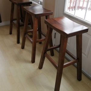 May include: Three wooden bar stools with a dark brown finish. The stools have a simple design with a curved seat and a sturdy base.
