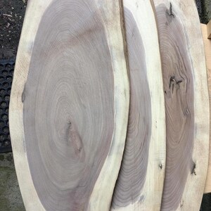 May include: Three oval-shaped wood slices with a light brown colour and a darker brown grain pattern. The wood slices are stacked on top of each other.