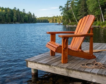 Puede incluir: Una silla Adirondack de madera con respaldo curvo y apoyabrazos anchos, con un acabado en tono marrón cálido. La silla está situada sobre un muelle de madera desgastada frente a un lago tranquilo rodeado por un denso bosque de pinos verdes.