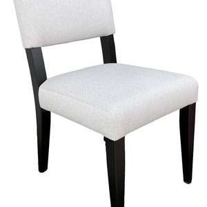 Peut inclure: Une chaise de salle à manger rembourrée de couleur blanche avec des pieds en bois noir. La chaise a un design simple et moderne.