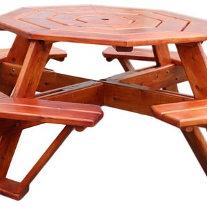 Può includere: Tavolo da picnic ottagonale in legno con sei panche. Il tavolo e le panche sono realizzati in legno massello e hanno una finitura naturale marrone rossiccia.