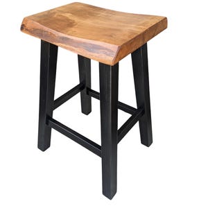 May include: A wooden counter stool with a natural wood seat and black legs. The seat has a curved design and a live edge. The stool is sturdy and suitable for kitchen or bar use.