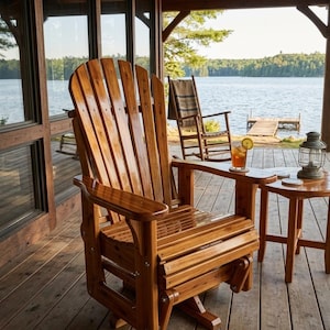 Puede incluir: Una silla deslizante de madera estilo Adirondack con respaldo alto y amplios reposabrazos. La silla es de madera marrón claro y está colocada en una terraza de madera con vistas a un lago. Una pequeña mesa auxiliar con una bebida y una linterna están cerca.
