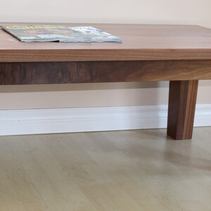 May include: A rectangular wooden coffee table with a dark brown finish. The table has four legs and a smooth, flat top. A magazine is placed on the table.
