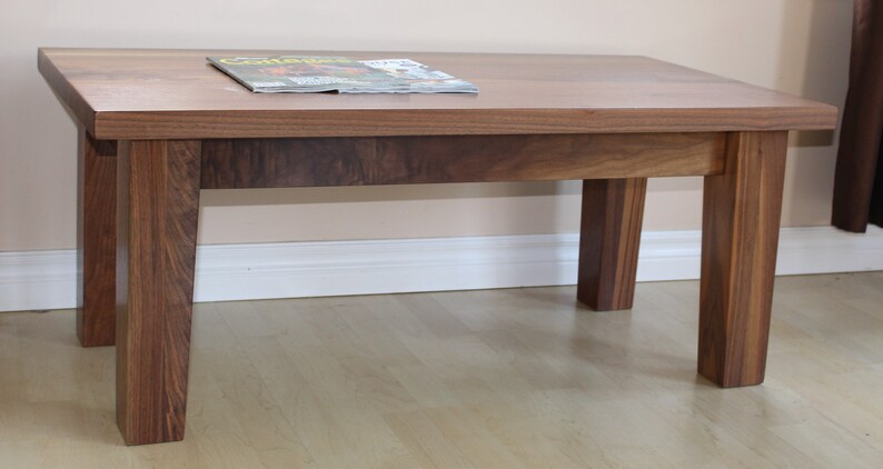 May include: A rectangular wooden coffee table with a dark brown finish. The table has four legs and a smooth, flat top. A magazine is placed on the table.