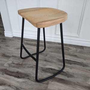May include: A wooden stool with a black metal frame. The stool has a natural wood finish and a simple design.