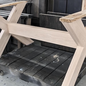 May include: A light wood table base with an X-shaped design. The base is made of unfinished wood and has a natural wood grain.