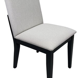 Puede incluir: Una silla de comedor con asiento y respaldo tapizados en gris claro. La silla tiene una estructura de madera negra y cuatro patas rectas. El diseño es simple y moderno, adecuado para varios estilos de interior.