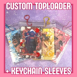 May include: Clear plastic keychain sleeves with decorative inserts. The sleeves are adorned with various designs, including a superhero, a portrait, and floral elements. The text "CUSTOM TOPLOADER" and "+ KEYCHAIN SLEEVES" are displayed in white.
