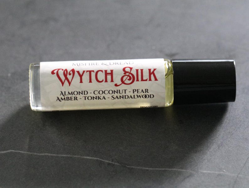 Puede incluir: Una peque&ntilde;a botella rectangular de vidrio de perfume "Wytch Silk" con tapa negra. La etiqueta muestra "MISTIRE & DREAD" sobre "WYTCH SILK" en escritura roja. Las notas de fragancia incluyen almendra, coco, pera, &aacute;mbar, haba tonka y s&aacute;ndalo.