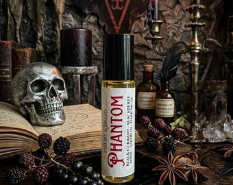 May include: A perfume bottle labelled "Phantom" with scent details, set on a dark wooden table with a skull, berries, and candles. The image has a gothic theme, with an open book and a pentagram symbol in the background.