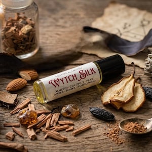 Puede incluir: Un frasco de perfume roll-on Wytch Silk con tapa negra y etiqueta blanca con texto rojo. Los ingredientes son almendras, coco, pera, &aacute;mbar, haba tonka y s&aacute;ndalo. El frasco est&aacute; rodeado de frutos secos, nueces y especias.