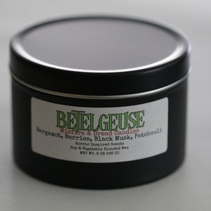 May include: Black metal tin candle with a white label that reads "BETELGEUSE Mistfire & Dread Candles Bergamot, Berries, Black Musk, Patchouli Horror Inspired Scents Soy & Vegetable Blended Wax NET WT. 8 OZ 266 (1)"
