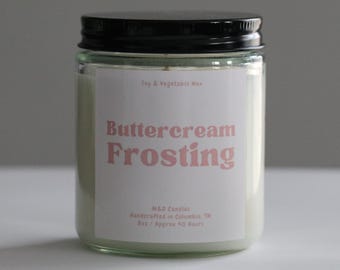 May include: A white candle jar with a black lid. The label reads "Buttercream Frosting" in pink lettering. The candle is made with soy and vegetable wax and has an approximate burn time of 40 hours.