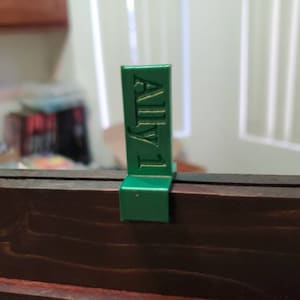 May include: A green plastic shelf label with the text "ALLY-1" printed in gold.