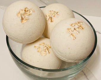 May include: Four white bath bombs with oatmeal flakes on top, in a clear glass bowl.